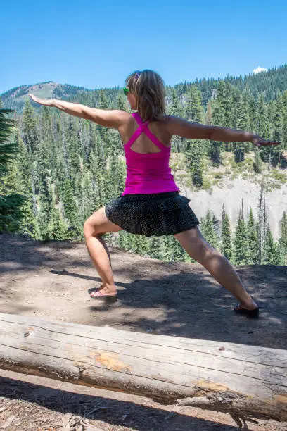 Woman doing a yoga pose mediation with arms up near the forest in Crater lake National Park in Oregon