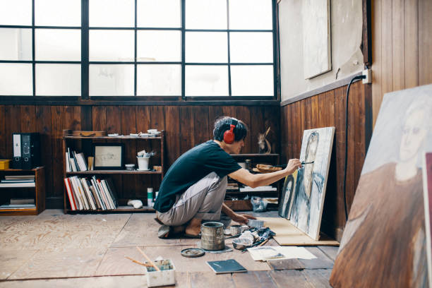 中年の男性がヘッドフォンを身に着けている間彼のスタジオで油絵絵画 - 画家 ストックフォトと画像