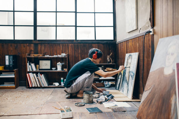 Mature man painting with oil paint in his studio while wearing headphones Mature man sitting on the floor painting with oil paint in his studio asian man headphones stock pictures, royalty-free photos & images