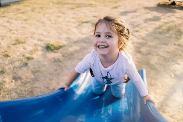 Lovely and carefree child enjoying her day at a park, playing on a slide at a playground.