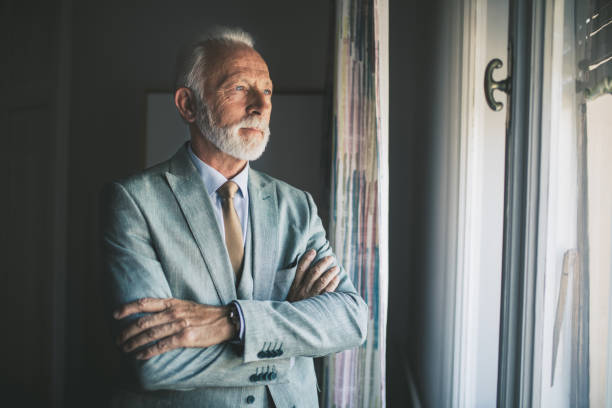 istock Senior man in suit looking through the apartment window 1061477530