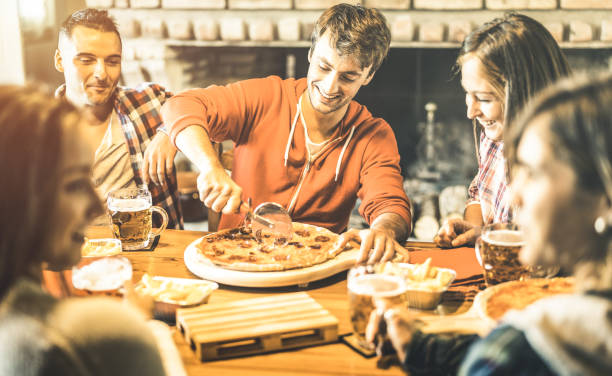 シャレー バー レストラン - 素朴なピッツェリア - 男のカット スライスを中心に本物の楽しい時間を一緒に楽しんで若い人たちと友情概念でピザを食べて幸せな友達グループ - pizza pizzeria friendship people ストックフォトと画像