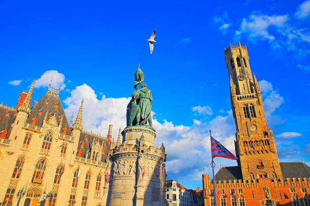 aves volando por encima de la torre del campanario de brujas y bandera belga en la plaza del mercado - bélgica - belfort fotografías e imágenes de stock