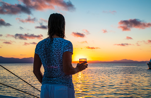 Mature lady holding a drink watching sunset