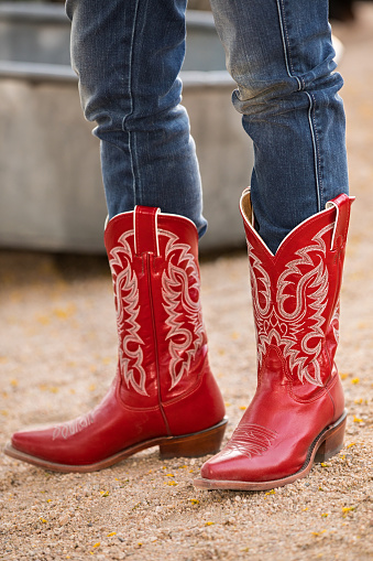 Closeup of female wearing jeans in red cowboy boots standing on a gravel road