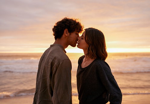 Shot of an affectionate young couple kissing on the beach at sunset