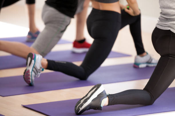 Close up of people legs sportive people doing lunge Slim people wearing sportswear and sneakers doing lunge standing on rubber carpet mat, close up humans lower body part. Sportive girls and guys perform exercises work on muscles of hips and buttocks man touching womans buttock stock pictures, royalty-free photos & images