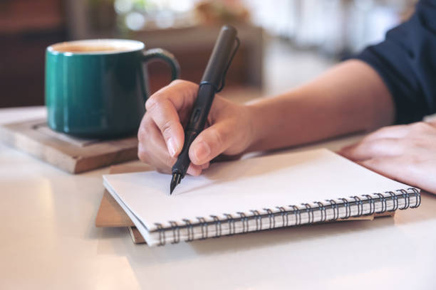 istock Closeup image of a woman's hand writing on blank notebook with coffee cup on table in cafe 1061571214