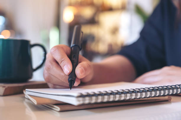 istock Closeup image of a woman's hand writing on blank notebook with coffee cup on table in cafe 1061571242
