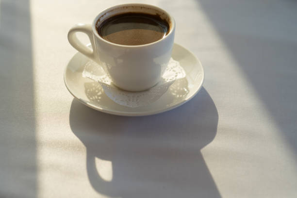 istock White coffee Cup on a table covered with a tablecloth in a beam of sunlight and long shadows 1061597990
