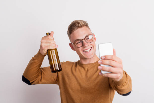 un joven hombre feliz con botella de cerveza en un estudio, tomar selfie. - vertical caucasian glasses red hair fotografías e imágenes de stock
