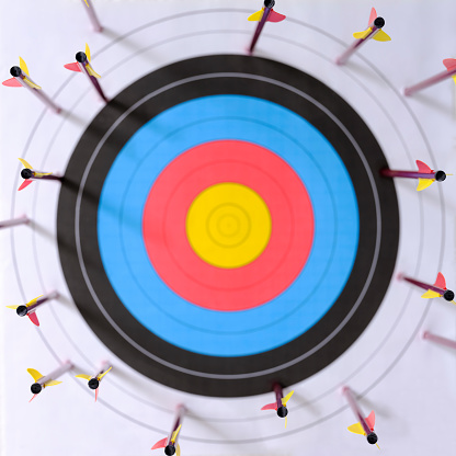 Many arrows around the edges of a sports target with a very low score relating to missing the target. Selective focus with the focus being on the back end of the arrows, with an out of focus target in the background. Concept image of being off target, weak strategy, poor aim, failure, out of reach etc.