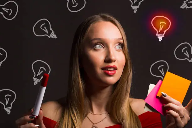 The girl holds a sticker and looks at the light bulb. Concept of brainstorming and searching for creative ideas using design thinking methods.