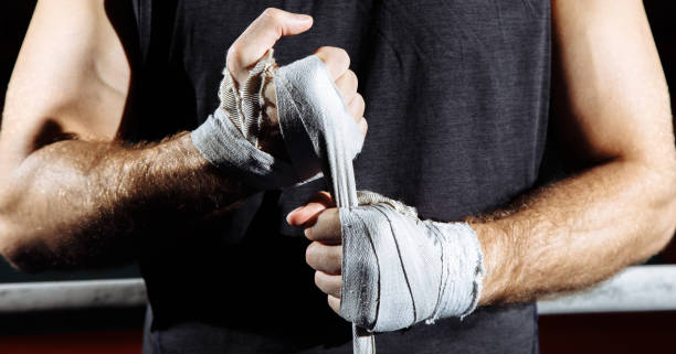 Strong man wrap hands on black background. Man is wrapping hands with boxing wraps, ready for training and active exercise. Strong man wrap hands on black background. Man is wrapping hands with boxing wraps, ready for training and active exercise wrestling sport stock pictures, royalty-free photos & images