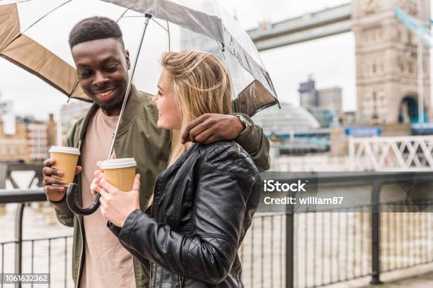 Happy Multiracial Couple Walking In London Holding An Umbrella Stock Photo - Download Image Now