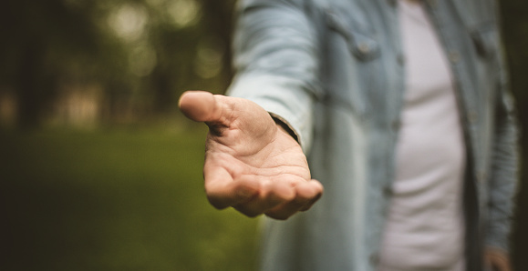 Help is always welcome. Young man in standing in park stretches his hand. Focus is on hand. Close up.