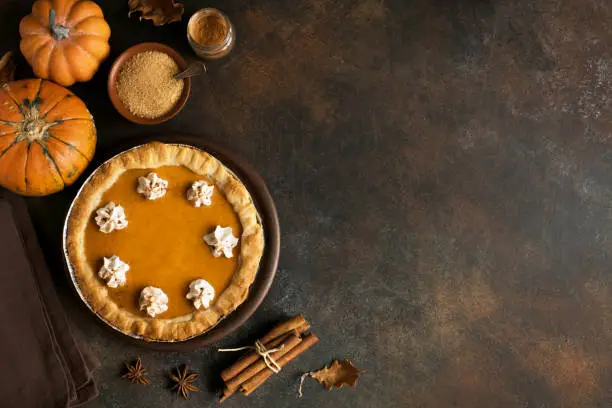 Pumpkin Pie with whipped cream and cinnamon on rustic background, top view. Homemade pastry for Thanksgiving traditional Pumpkin Pie.