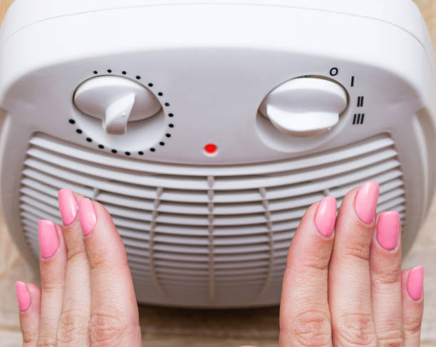 Female warms her cold hands near an electric heater at home. Selective focus, part of body. Female warms her cold hands near an electric heater at home. Selective focus, part of body. warms stock pictures, royalty-free photos & images