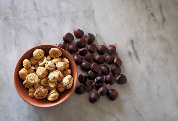 castagne sgusciate essiccate su una tavola di marmo con altre appena raccolte. - chestnut sweet food yellow group of objects foto e immagini stock