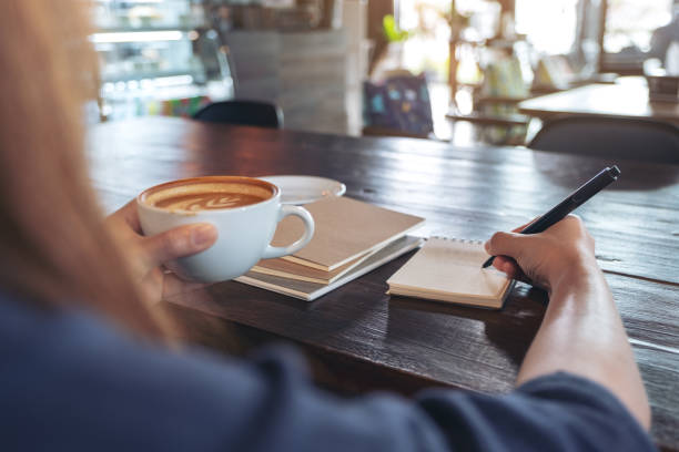 istock Closeup image of a woman writing on blank notebook while drinking coffee in cafe 1061641958
