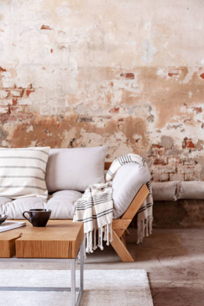 Blanket on wooden sofa in minimal loft interior with table and red brick wall. Real photo