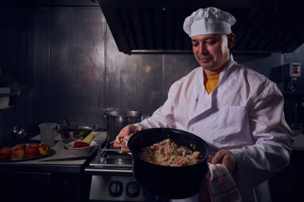 Professional chef cook in a white apron and cooks hat prepairing delicious meal on a kitchen.
