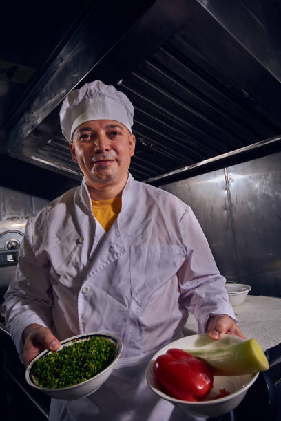 Professional chef cook in a white apron and cooks hat prepairing delicious meal on a kitchen.