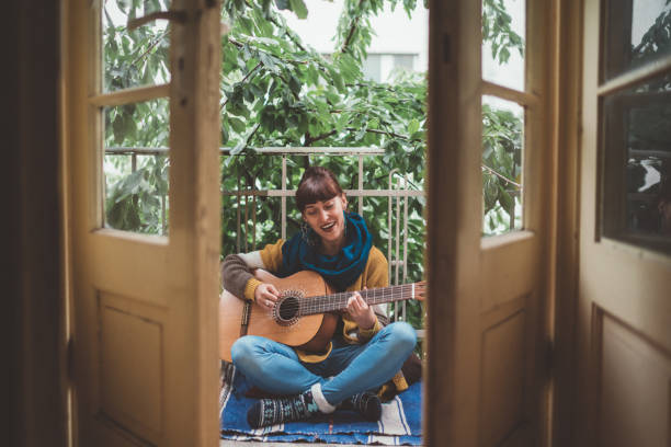 Hippie woman playing the guitar at home Young woman just playing the guitar at terrace legs crossed at ankle stock pictures, royalty-free photos & images