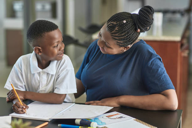 Happy woman looking at son doing homework Happy woman looking at son doing homework in living room. Smiling boy is studying by mother at table. They are at home. short weave hairstyles stock pictures, royalty-free photos & images