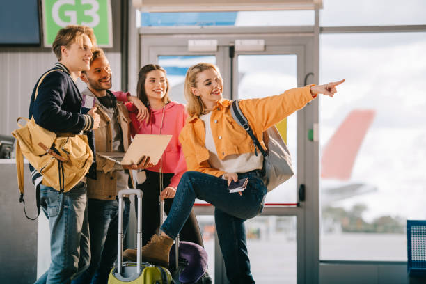 istock smiling young friends using laptop and pointing away while waiting for flight in airport 1061661688