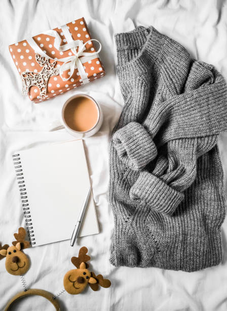 istock Christmas planning background - coffee cup, clean notepad, gift box, cozy gray knitted sweater on the bed. Top view, flat lay 1061666558
