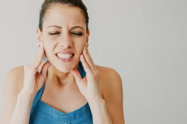 Annoyed young woman suffering from toothache and touching jaw. Irritated girl with closed eyes gritting teeth from pain. Hurt concept