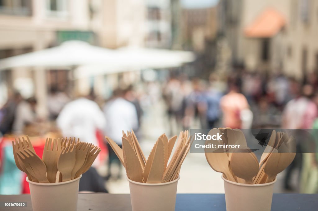 Disposable Wooden Cutlery – Eco Friendly Biodegradable Forks Spoons Knives In the front of the photography is Disposable Wooden Cutlery – Eco Friendly Biodegradable Forks, Spoons, Knives. In the background is party on the street with plenty of people. Environmental Conservation Stock Photo