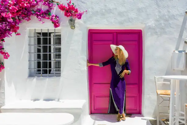 Attractive, blonde traveler woman in front of a traditional cylcadic house on the island of Paros, Naoussa, Greece