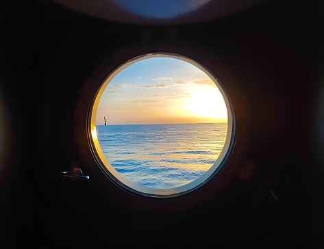 A peacefull view through porthole of a sailing vessel in calm seas at sunset