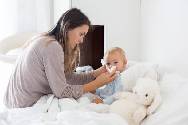 Mother and baby in pajamas, early in the morning, mom taking care of her sick toddler boy Mother and baby in pajamas, early in the morning, mom taking care of her sick toddler boy. Baby in bed with fever and running nose illness in babies stock pictures, royalty-free photos & images