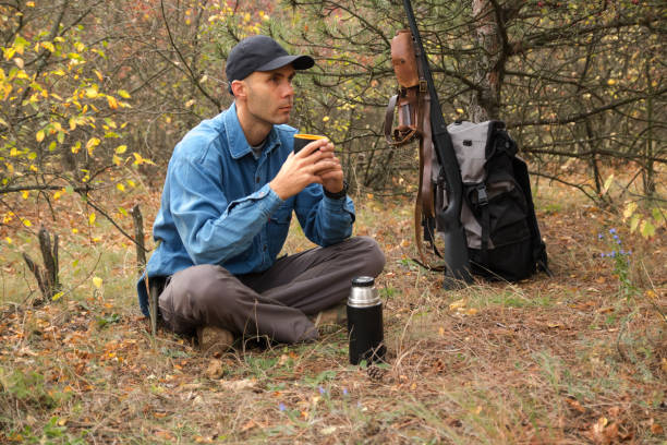 istock caucasian male hunter resting in forest. drinking tea from thermos. shotgun, ammunition, backpack on the background 1061684696