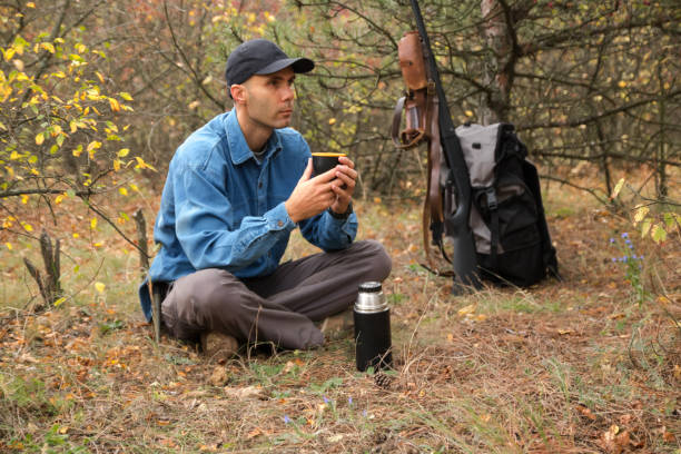 istock caucasian male hunter resting in forest. drinking tea from thermos. shotgun, ammunition, backpack on the background 1061684742