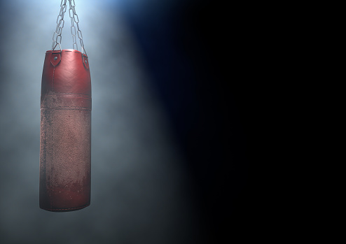 An old worn red leather punching bag hanging by chains in a 