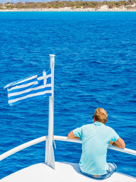 griechische flagge winken am bug eines bootes in richtung der insel chrissi oder in der karibik in griechenland segeln - chrissy stock-fotos und bilder