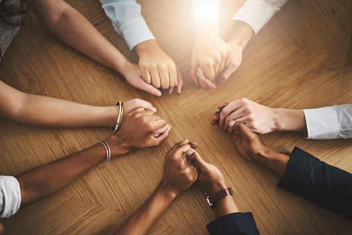 Closeup shot of a group of businesspeople sitting together at a table and holding hands