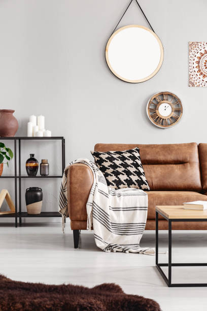 istock Vertical view of warm ethno living room with leather couch with patterned pillow and mirror and clock on beige wall, real photo 1061701038