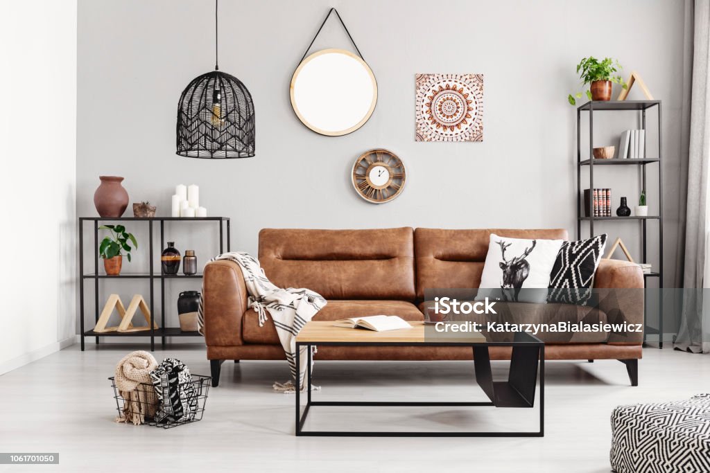 Leather sofa with pillows and blanket in the middle of elegant living room interior with metal shelves and modern coffee table, real photo Sofa Stock Photo