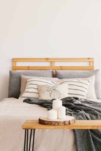 istock Three candles on the wooden table next to cozy bed with patterned pillows and grey blanket, real photo with copy space on the wall 1061703736