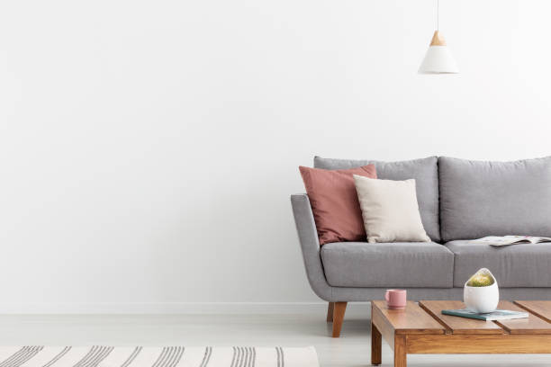 istock Pillows on grey settee and wooden table in white apartment interior with copy space on the wall. Real photo 1061707624