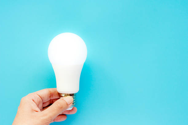 istock Hand holding glowing LED light bulb on blue background for energy savings concept 1061711906