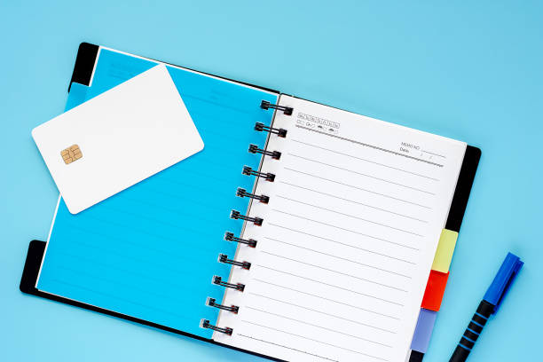 istock Blank white credit chip card, spiral notebook and a pen on blue background for spending plan concept 1061712964