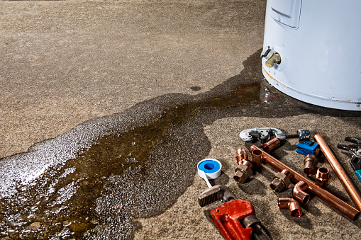 Un grifo con fugas en un calentador de agua doméstico con herramientas y accesorios para reemplazar el aparato photo
