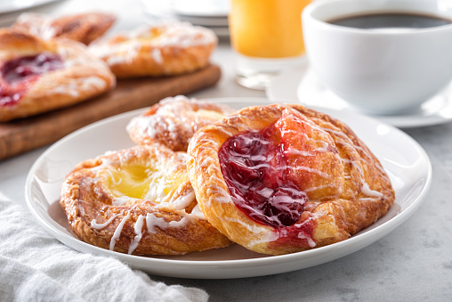 Delicious cherry and lemon mini danishes on a marble table top with black coffee and orange juice.