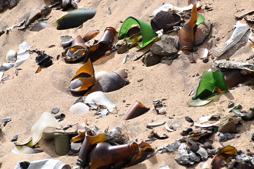 Coloured broken glass sticks out form the sand and garbage at the Terrace Bay garbage dump.\n\nThe photo is taken at Terrace Bay inside the Skeleton Coast National Park, Namibia. The area is accessible with a permit. Terrace Bay is the furthest north you can drive, inside the Skeleton Coast National Park. The photo was taken in February 2018